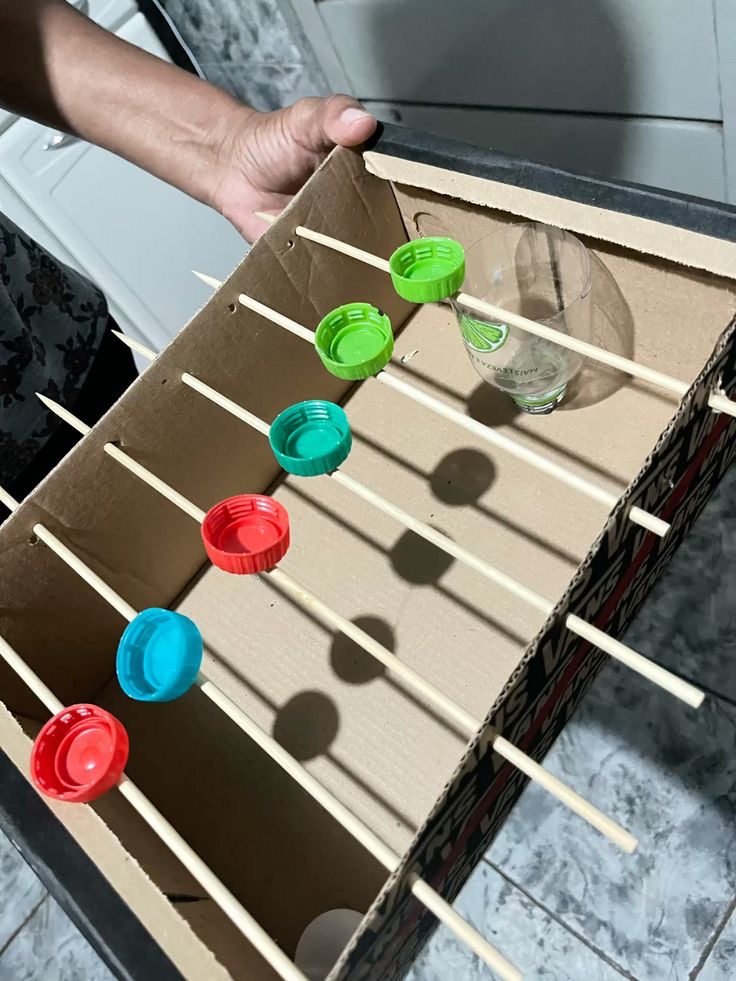 Labirinto construído com caixa de papelão, palitos e tampinhas coloridas